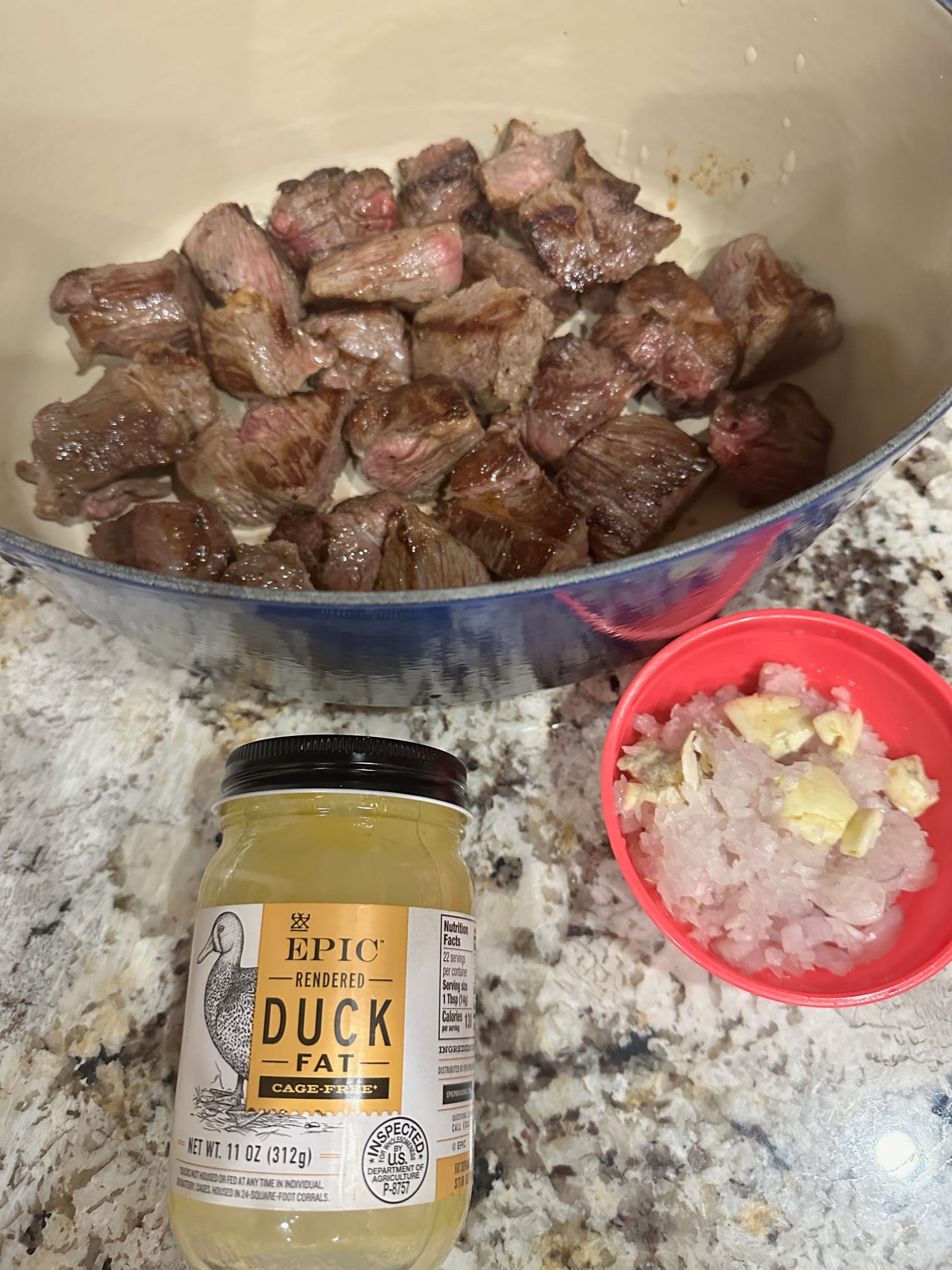 A Picture showing beef along with a small bowl of onions and garlic and a jar of Duck Fat