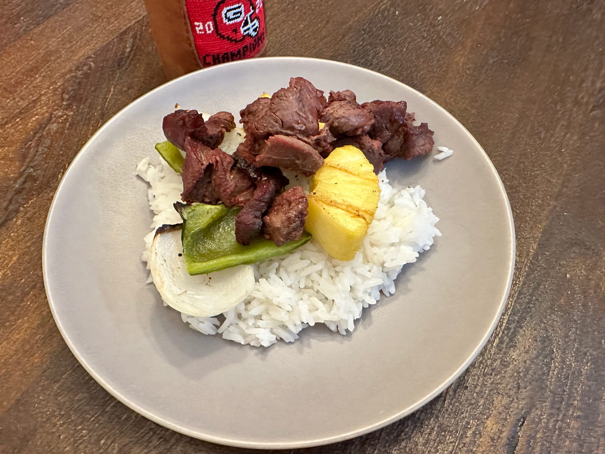 A picture of a plate containing a bed of Jasmine Rice,  some kebab meat with peppers, onions and a piece of pineapple